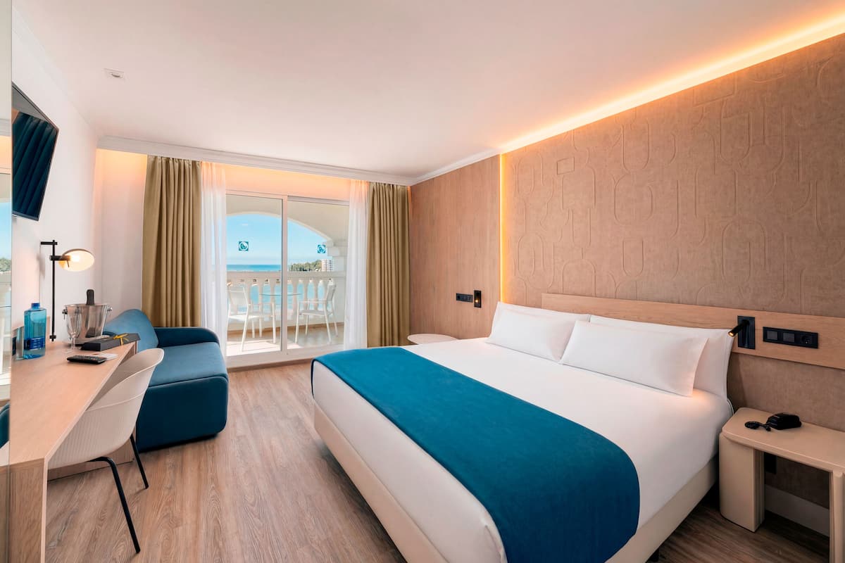Une chambre d’hôtel équipée d’un lit, d’un bureau, d’une chaise, d’une petite table, d’une télévision et d’un balcon avec vue.