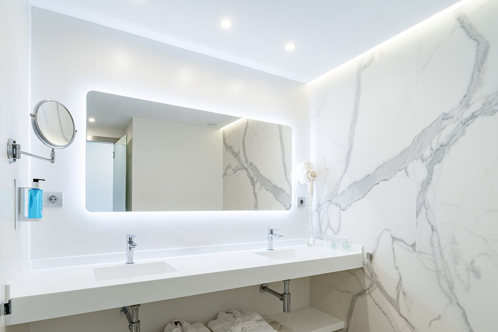 Une salle de bain moderne avec un grand miroir, deux lavabos, un porte-serviettes et un sèche-cheveux.