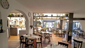 An interior view of a restaurant with multiple dining tables, chairs, and a kitchen area visible through an archway. - Puerto Caleta (Antigua)