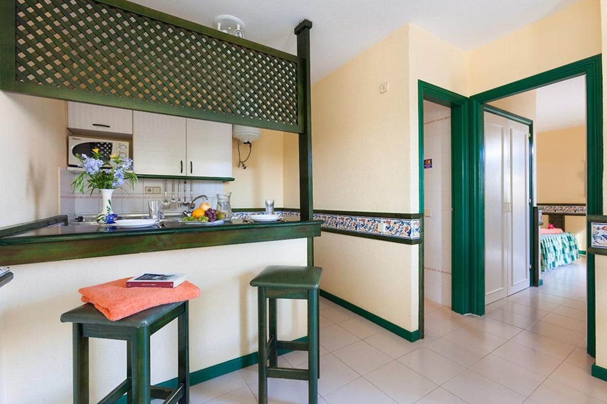 A kitchen with a green countertop, two stools, and a decorative wall panel.