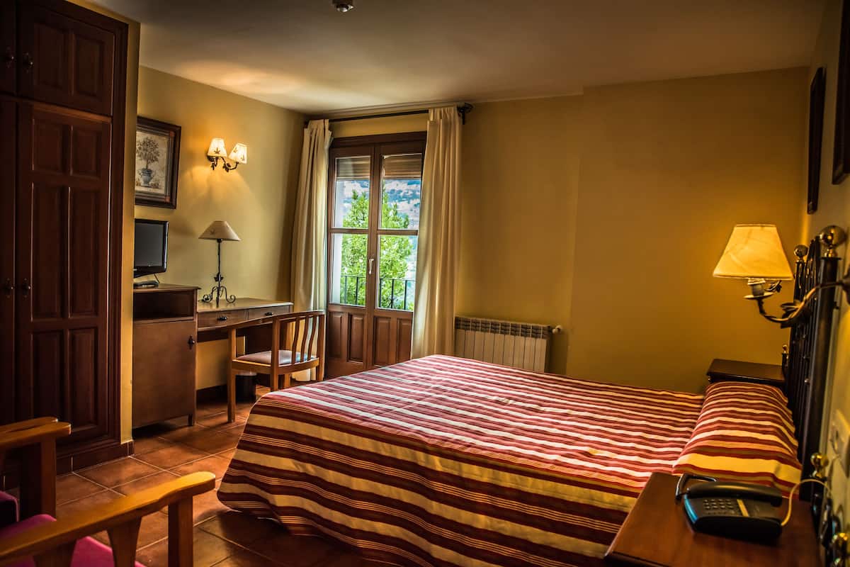 Ein Hotelzimmer mit Bett, Schreibtisch, Stuhl und einem Fenster mit Vorhängen.