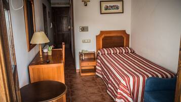 A small, neatly arranged bedroom with a single bed, a bedside table, a lamp, and a chair.