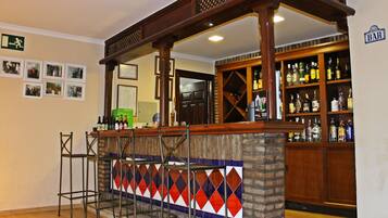 A bar area with a wooden counter, shelves with bottles, and a patterned wall.