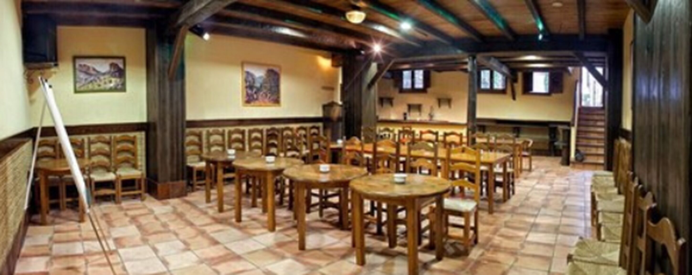 Un amplio comedor con mesas y sillas de madera, techos altos con vigas a la vista y obras de arte en las paredes.