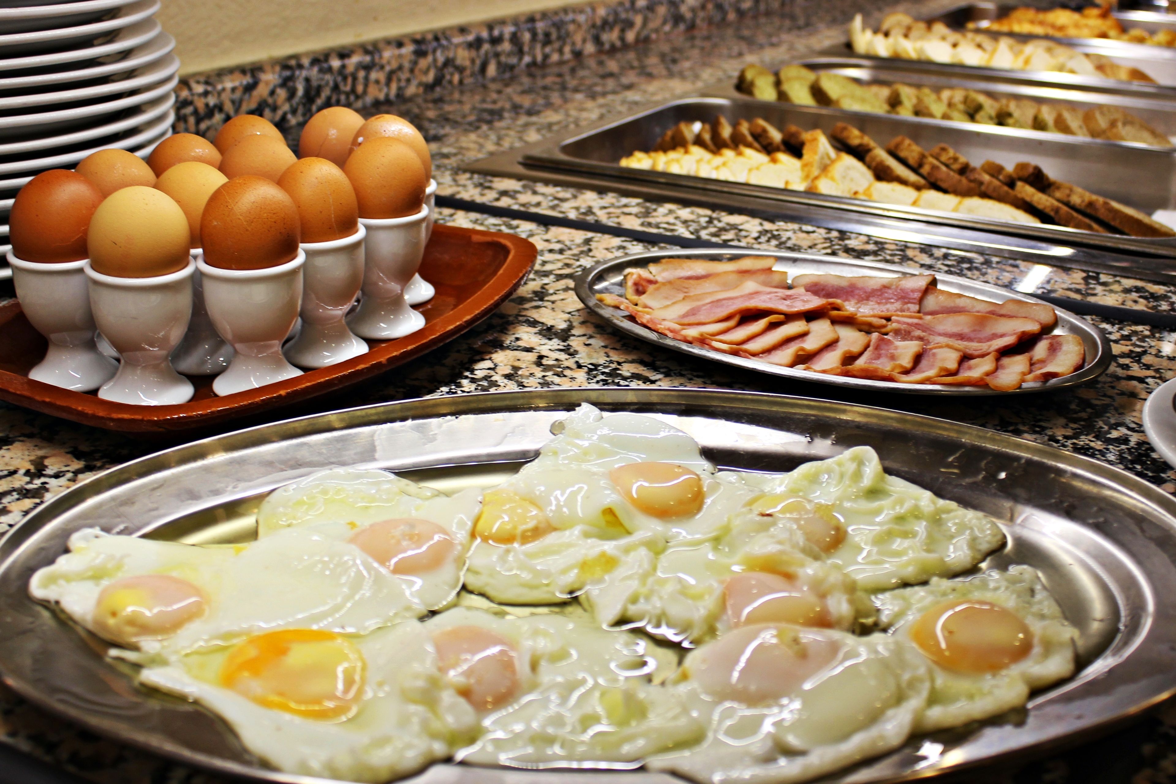 Ein Buffet mit verschiedenen Speisen, darunter Eier, Speck und weitere Frühstücksoptionen.