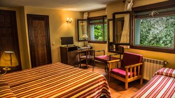 Une chambre d’hôtel avec deux lits, un bureau avec un ordinateur, une chaise et une fenêtre donnant sur un paysage verdoyant.