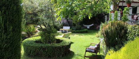 A well-maintained garden with a lawn, a wooden bench, and a white chair.