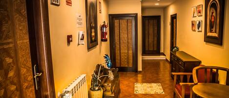 A hallway with a radiator, a fire extinguisher, a framed picture, a door, and a small table with a chair.