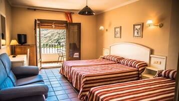 Quarto de hotel com duas camas, um sofá, uma TV e uma varanda com vista para as montanhas.