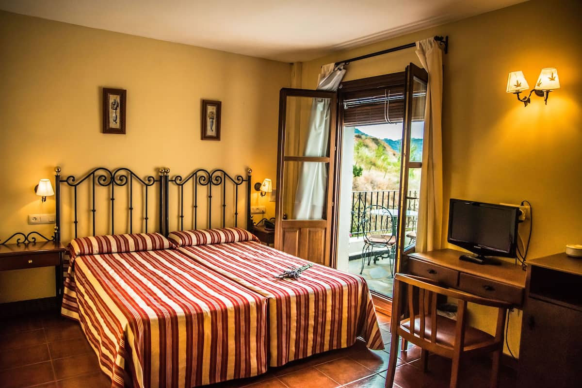 Ein Hotelzimmer mit Bett, Schreibtisch mit Fernseher und Balkon mit Blick ins Grüne.