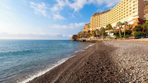 A coastal hotel with a rocky beach, clear blue sky, and a large building with multiple balconies. - Mirador del Cabo Hotel Adults Recommended (Enix)