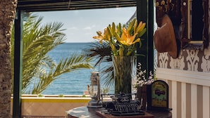 A view of the ocean through a window, a vase with flowers, a vintage radio, and a lantern on a table. - Mirador del Cabo Hotel Adults Recommended (Enix)