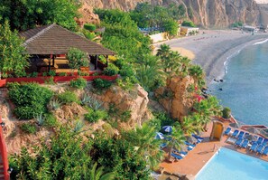 Un complejo turístico frente a la playa con piscina, sillas de descanso y restaurante.