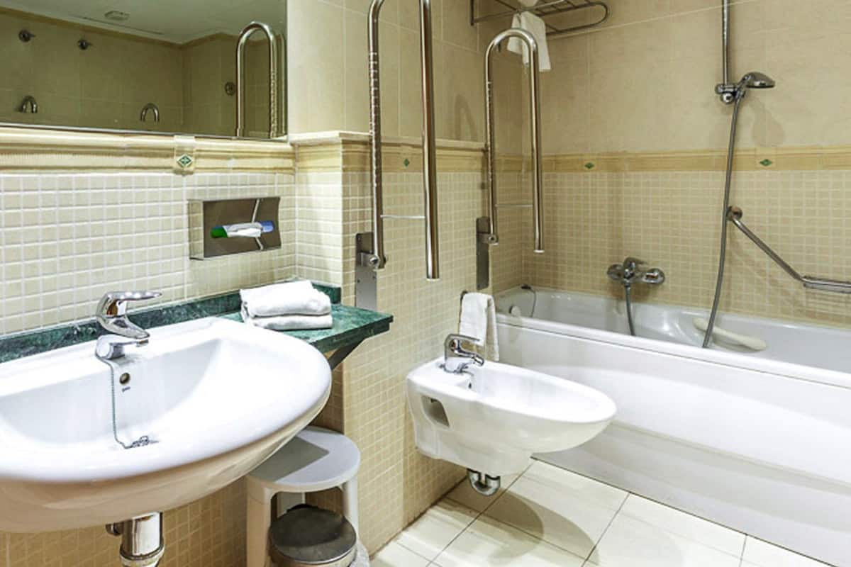 A bathroom with two sinks, a bidet, a bathtub, and a shower with grab bars.