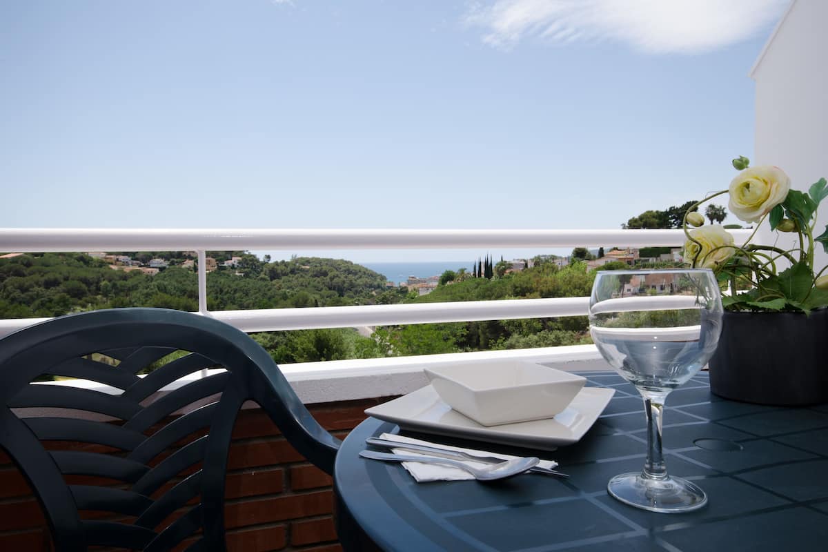 Une table avec un verre d’eau, un bol blanc et une plante en pot, le tout placé sur un balcon donnant sur un paysage magnifique.