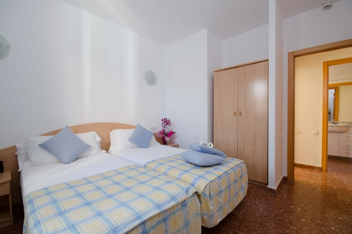 Un lit double avec une couvre-lit à carreaux, une armoire en bois et une petite table de chevet avec une lampe.