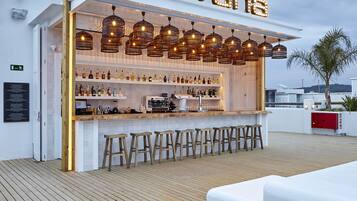 Un bar con fachada blanca, taburetes de madera y una variedad de botellas.