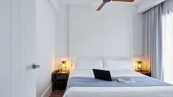 Un dormitorio con una cama, un ventilador de techo, lámparas de noche, una computadora portátil y un par de zapatos en el suelo.
