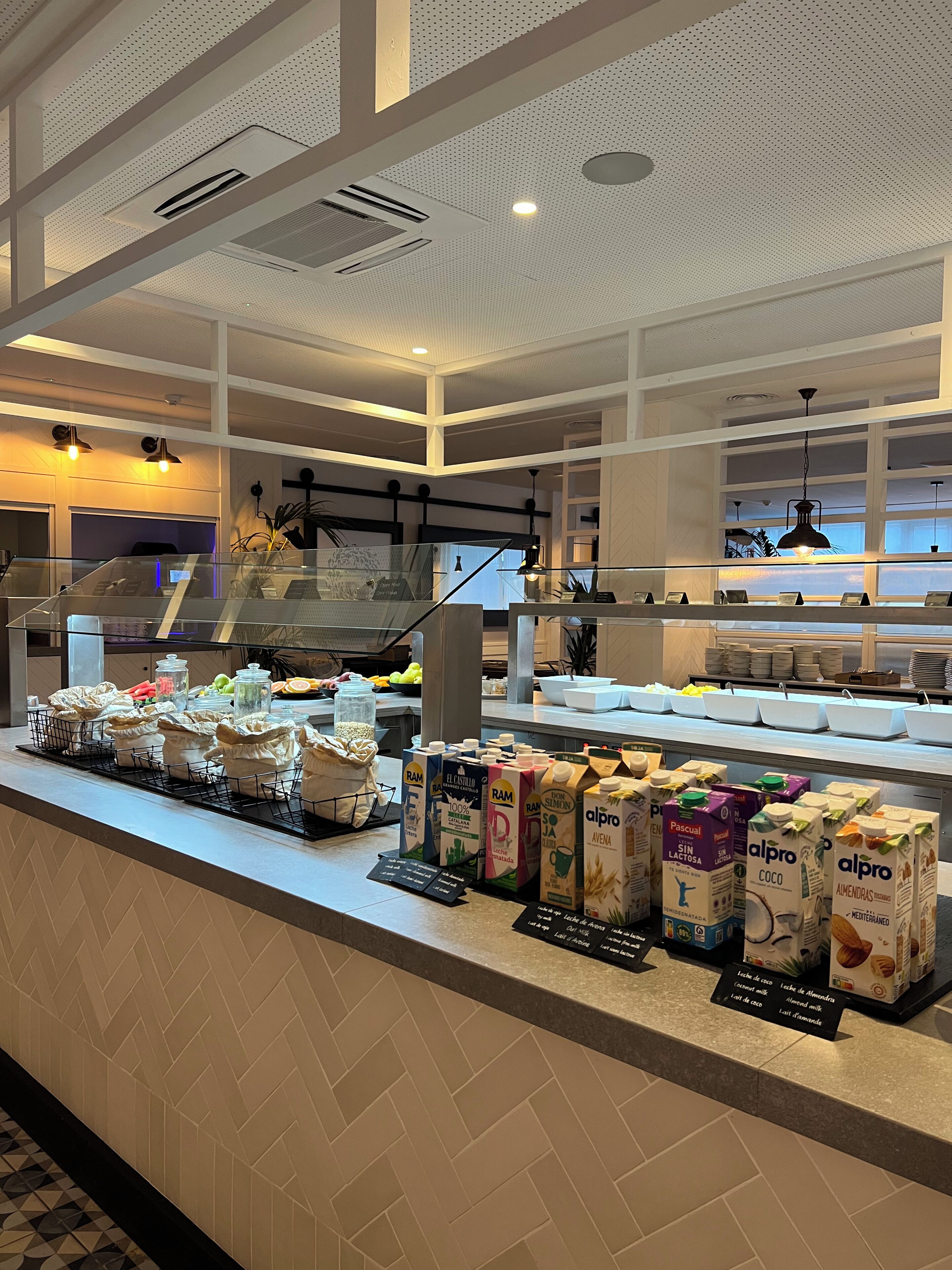 Zona de bufé con diversas opciones de comida y bebida, incluyendo cartones de leche y jugo, y una vitrina con alimentos.