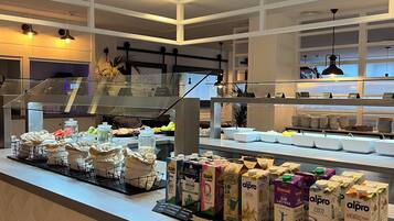 Zona de bufé con diversas opciones de comida y bebida, incluyendo cartones de leche y jugo, y una vitrina con alimentos.