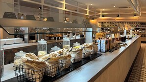 Zona de buffet con alimentos y recipientes sobre una encimera, suelo de baldosas e iluminación empotrada en el techo.