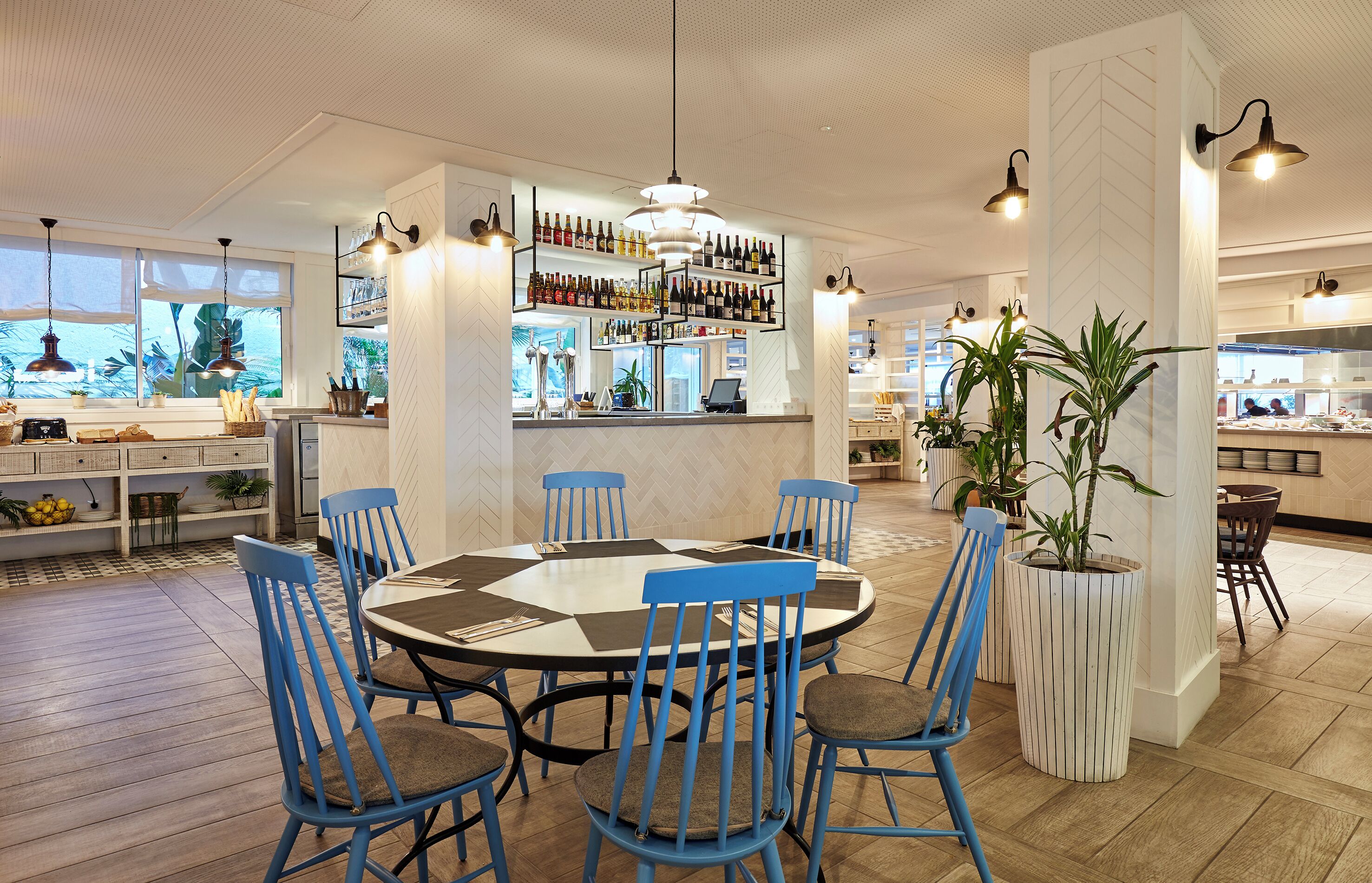 Un espace repas moderne avec une table ronde, des chaises bleues et un bar doté d’étagères remplies de bouteilles.