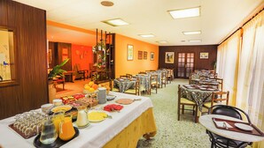 Zona de dinar amb taules preparades per esmorzar, un bufet amb diferents aliments i una finestra gran amb cortines.