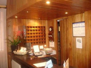 A wooden reception desk with a computer, telephone, and various papers. - Santa Ana (Lloret de Mar)