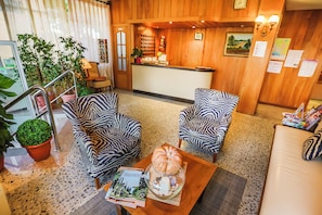 A reception area with a wooden reception desk, two zebra-striped armchairs, a coffee table with a pumpkin centerpiece, and a potted plant. - Santa Ana (Lloret de Mar)