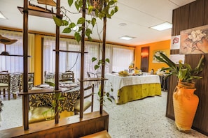 A dining area with tables, chairs, and a large potted plant. - Santa Ana (Lloret de Mar)