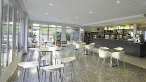 Un comedor moderno con mesas redondas y sillas blancas, una barra con exhibición de bebidas y ventanas amplias que ofrecen vistas al exterior.