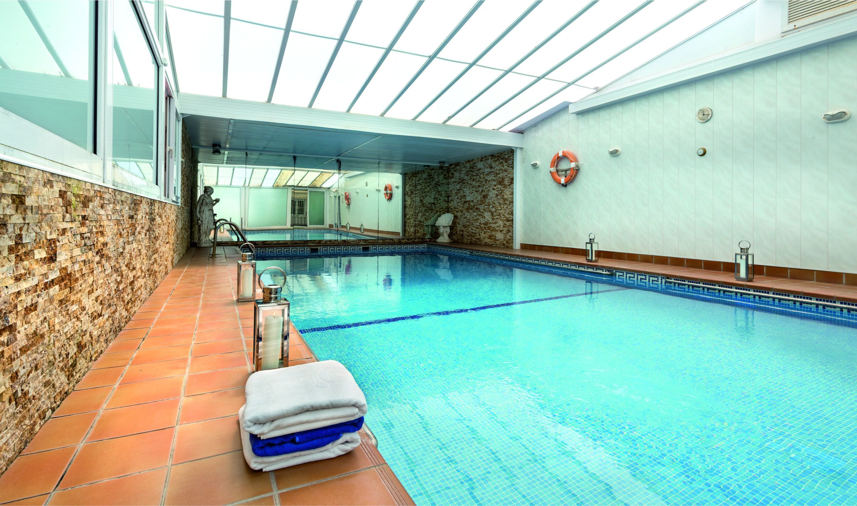 Una piscina interior con agua azul cristalina, una pared de piedra en un lateral y suelo de baldosas.
