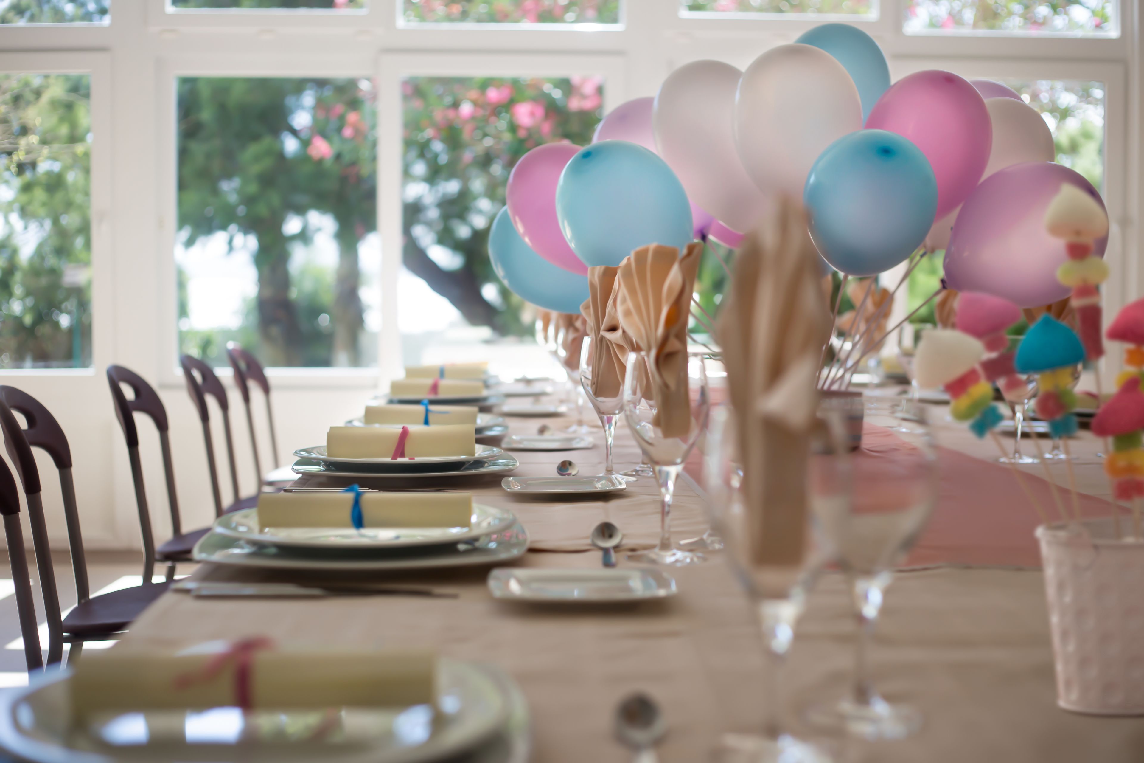 Ein Esstisch, gedeckt mit Tellern, Gläsern und einer Torte, verziert mit Luftballons und einer Blumenvase.