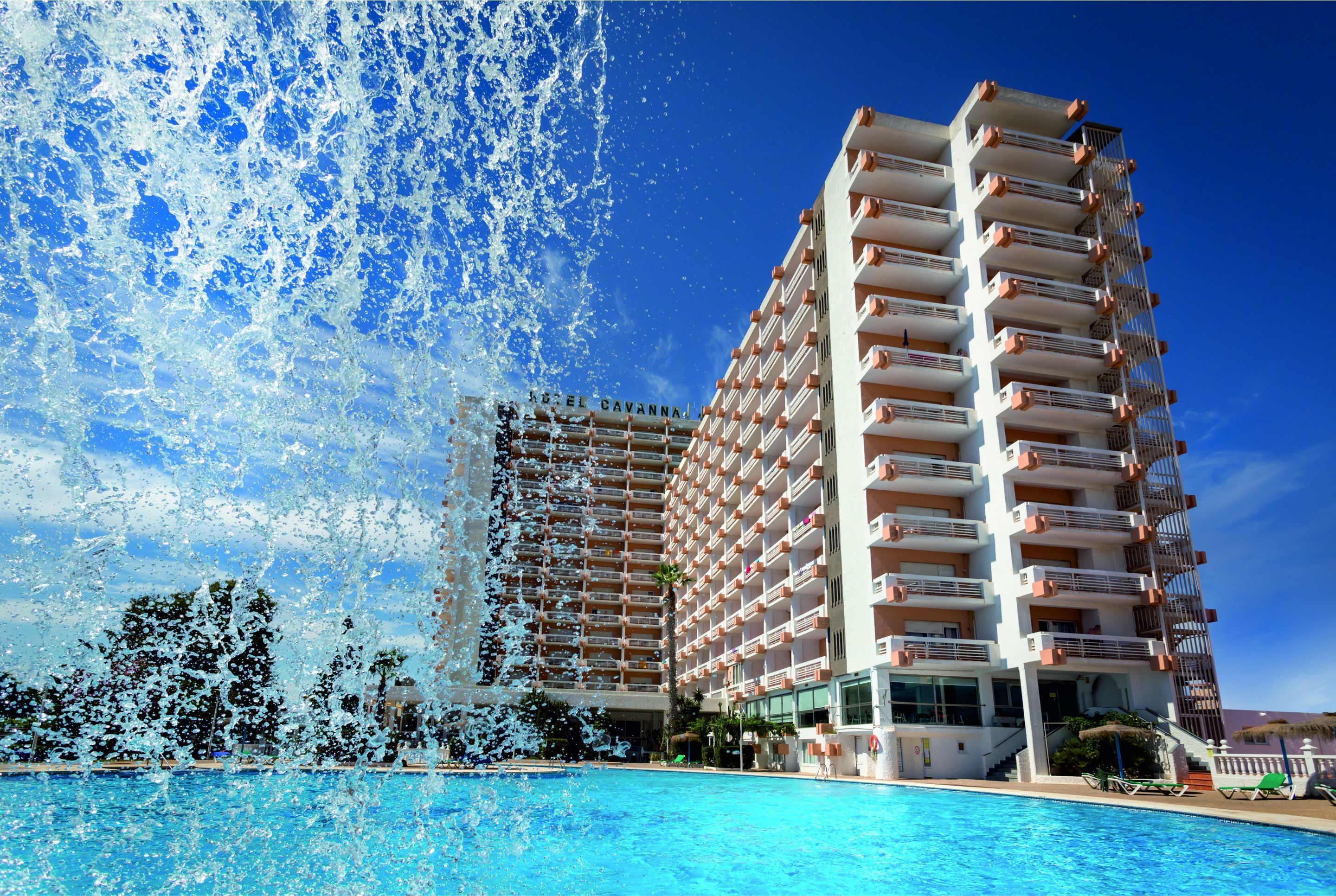 A hotel with multiple balconies, a swimming pool, and a clear blue sky.
