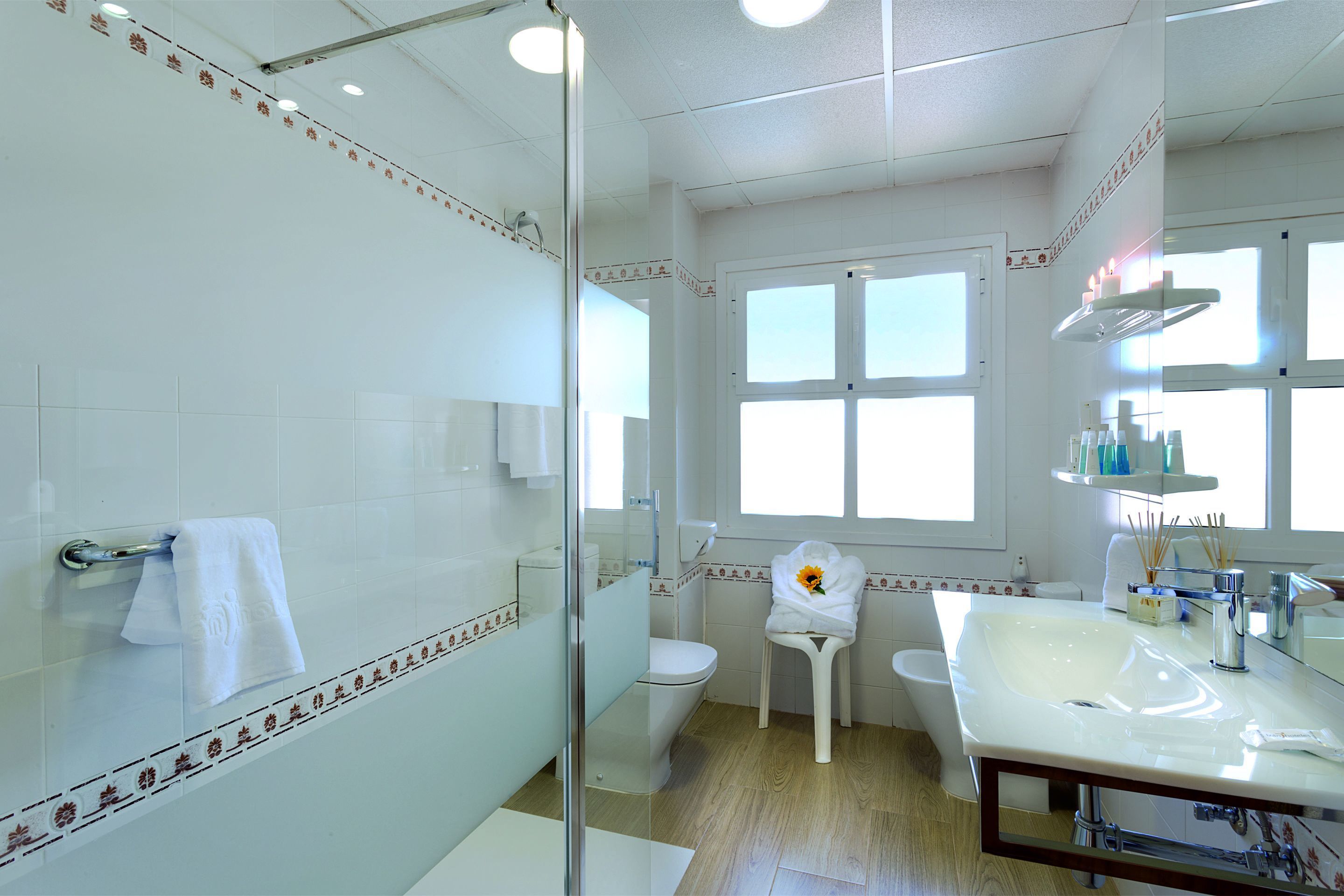 Une salle de bain avec une douche à parois de verre, des toilettes, un lavabo avec un miroir et une fenêtre.