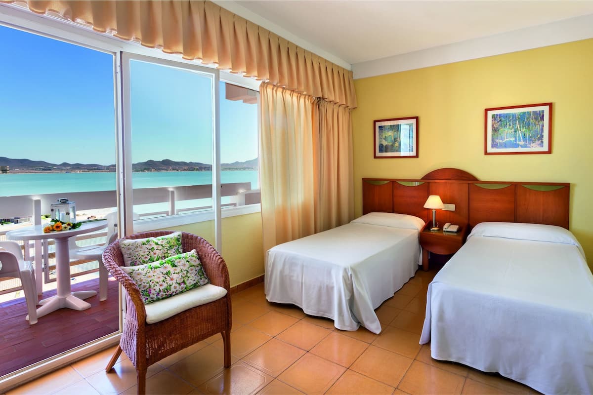 Ein Hotelzimmer mit zwei Betten, einem Balkon mit Tisch und Stühlen und Blick aufs Meer.
