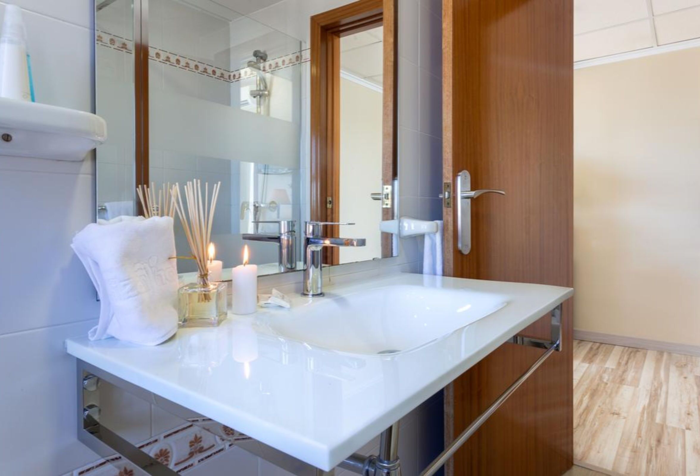 Un baño moderno con un lavamanos blanco, un espejo y una puerta de madera.
