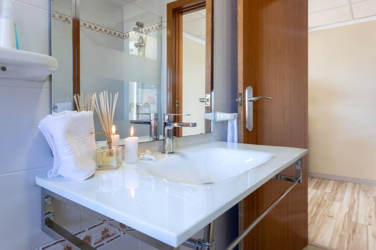 Un baño moderno con un lavamanos blanco, un espejo y una puerta de madera.
