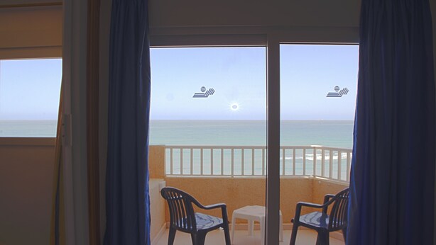 A balcony with two chairs and a small table, overlooking the sea.