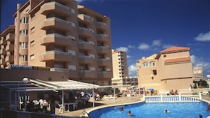 A hotel with a swimming pool, outdoor seating, and multiple balconies.