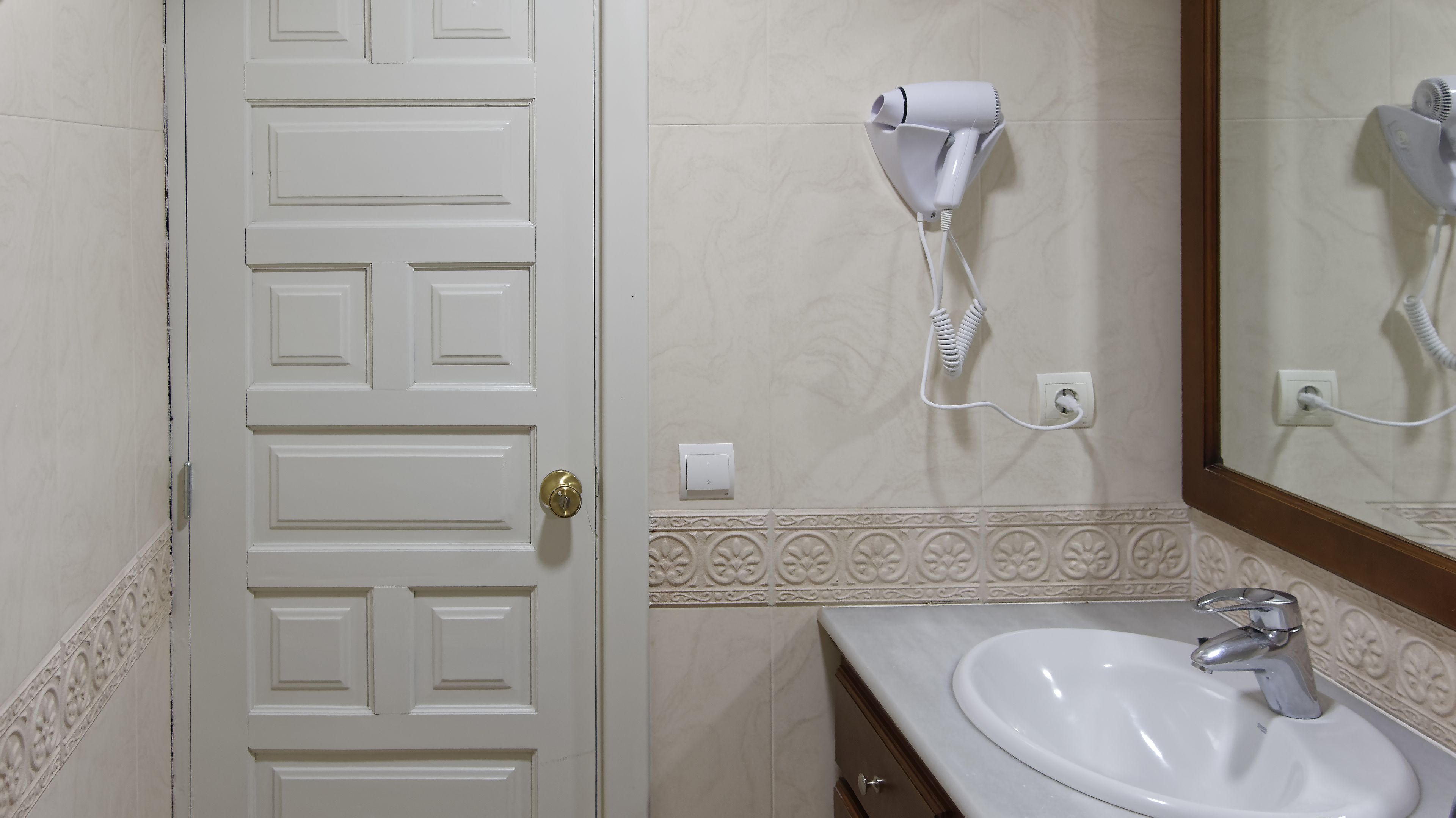A bathroom with a white door, a hairdryer on the wall, and a sink with a mirror above it.