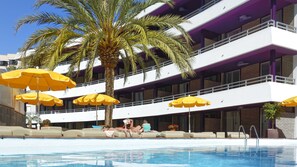 A hotel with a pool area, multiple balconies, and yellow umbrellas.