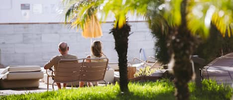 A couple sitting on a bench in a garden area with a palm tree and a wall in the background.