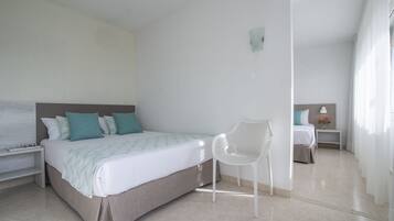 A modern bedroom with a bed, a white chair, a nightstand, and a small table with a lamp and flowers.