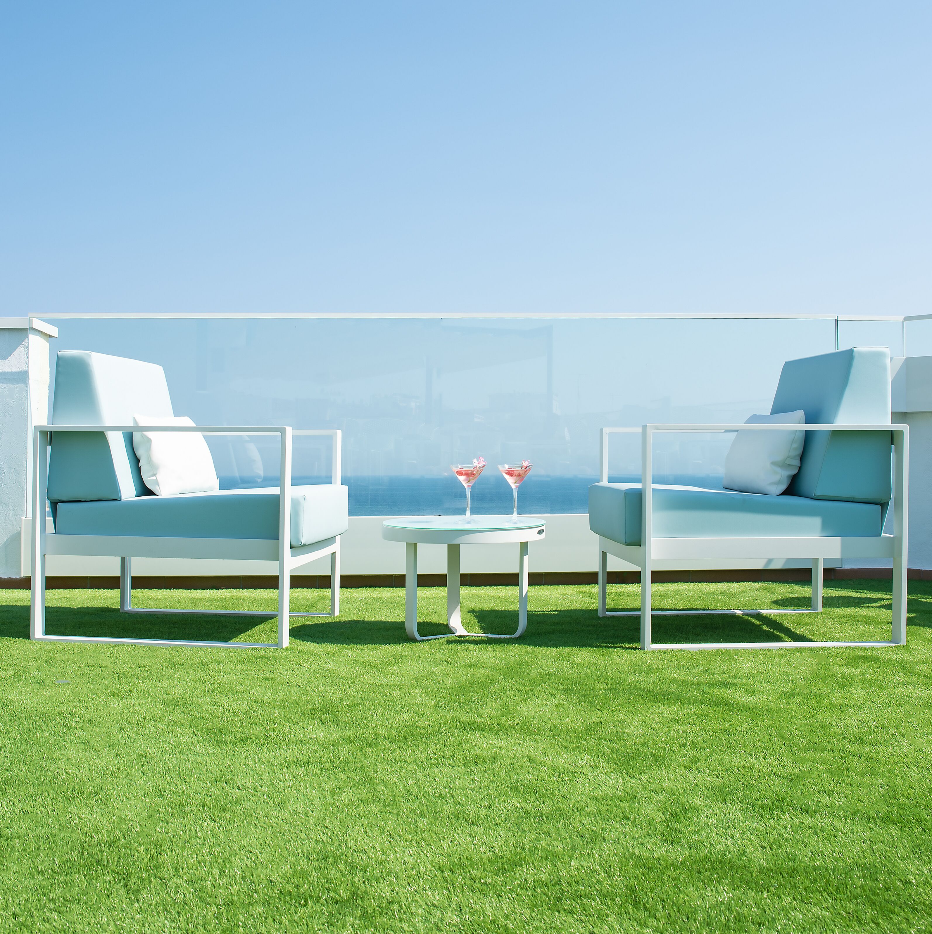 A modern outdoor seating area with two white lounge chairs and a small table, featuring a clear view of the ocean.