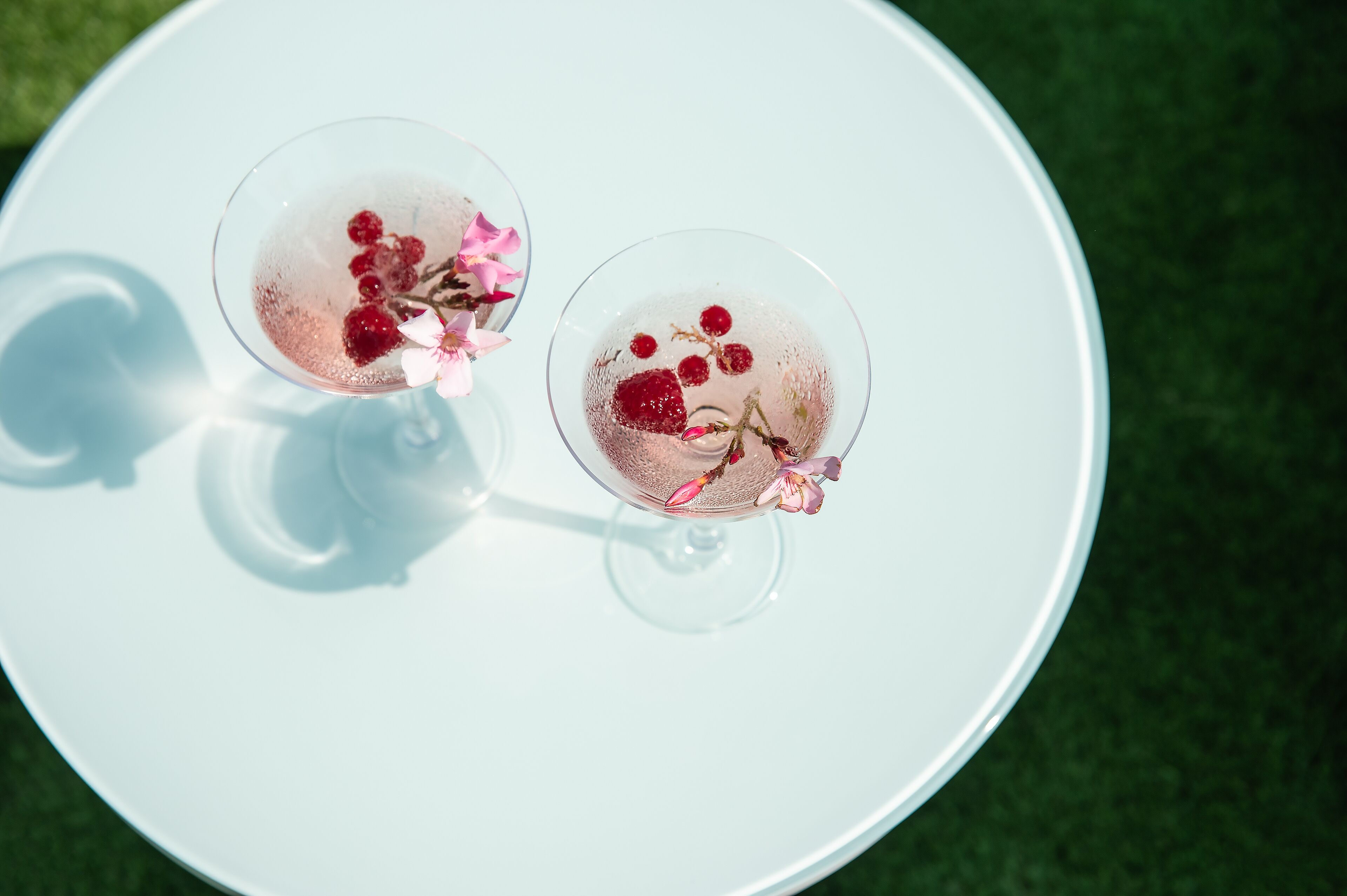 Deux verres d’une boisson rose, agrémentée de fruits rouges et de fleurs, posés sur une assiette blanche.