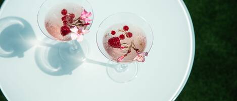 Deux verres d’une boisson rose, agrémentée de fruits rouges et de fleurs, posés sur une assiette blanche.