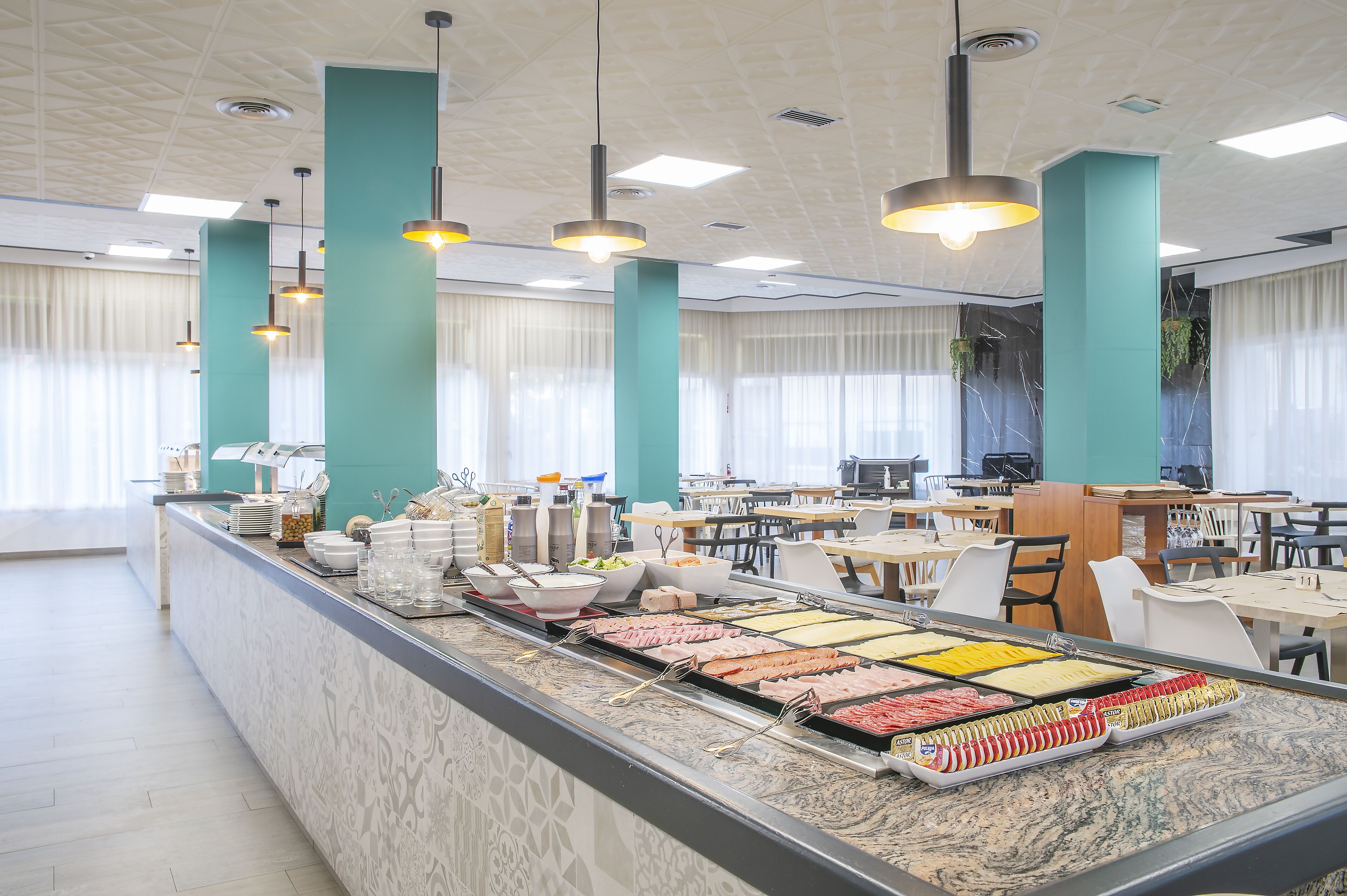 Un espace buffet proposant une variété de plats, un coin repas avec des tables et des chaises, et un plafond doté d’un éclairage encastré et d’éléments décoratifs.