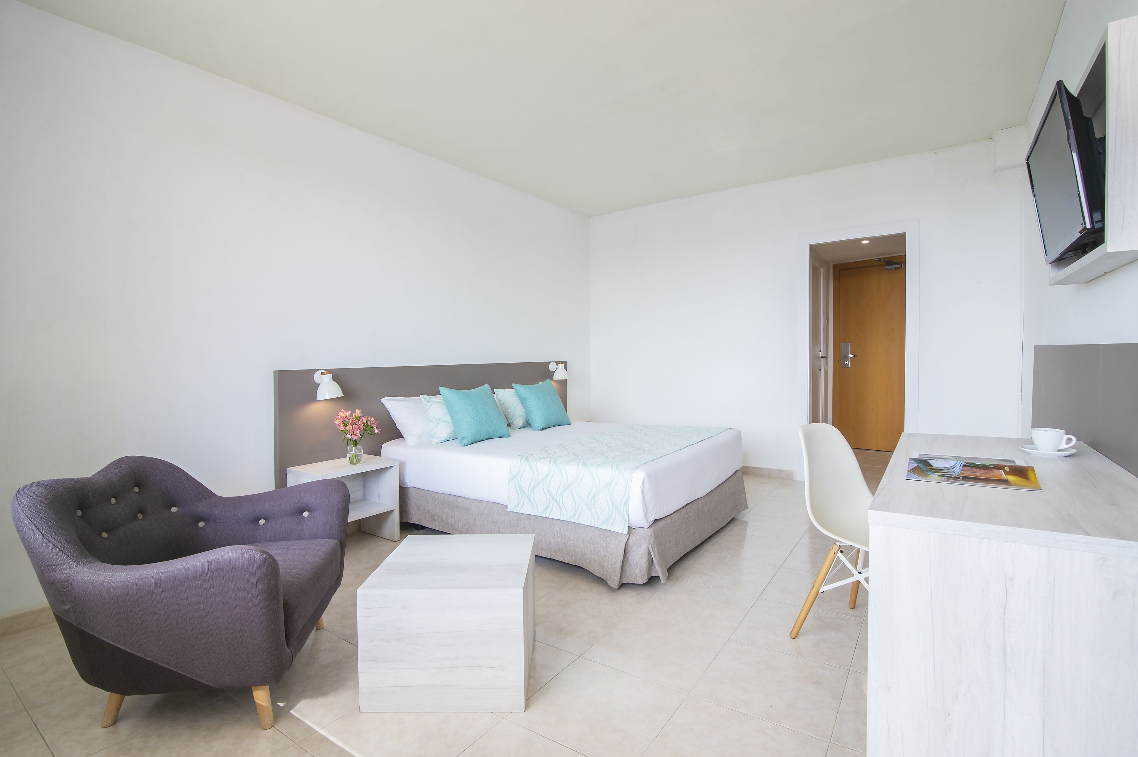 A modern hotel room with a bed, a chair, a desk, and a television.