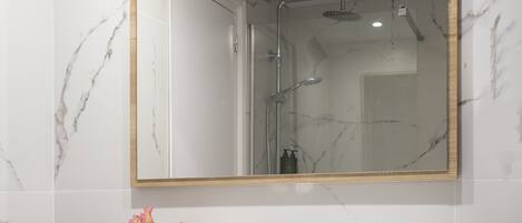 A bathroom with a marble-tiled wall, a wooden vanity with a white sink, a mirror, and a towel shelf.